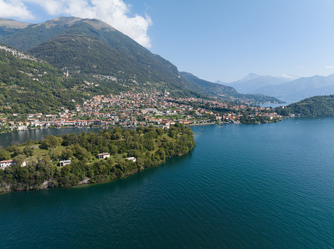 Aerial view over the small town of Ossuccio and the Isola Comacina on the shores of Lake Como in Italy. Lake Como is an Iconic lake destination known for its scenic beauty, mountain vistas & historic lakeside residences.