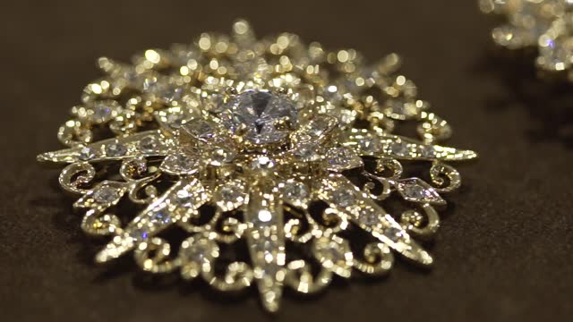 Gold brooch decorated with diamonds ornaments laying on a black floor
