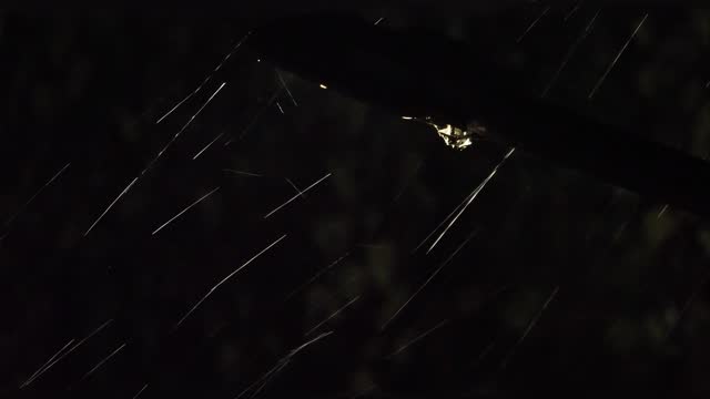 Raindrops illuminated by a street lamp during a downpour on a dark background. Real rain sound