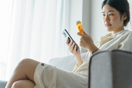 Asian woman Search for information on Internet in smartphone with holding bottled drug. girl reading information online on mobile phoneÂ medicine healthcare product concept.