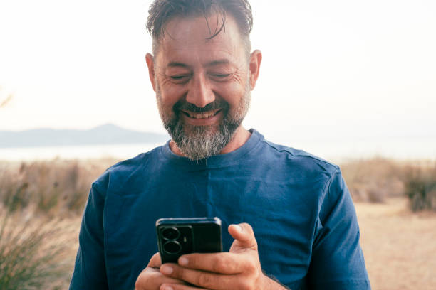 istock Front view of one casual man using mobile phone with cheerful smile expression on face. Modern traveler people with connection and communication technology. Texting and messaging outdoor cellphone 1714415835