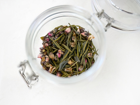 Top view of tea leaf blend flavor with dried red flowers petals, silver needle white rose tea, spring drink, organic in glass jar, pure and aroma antioxidant drink