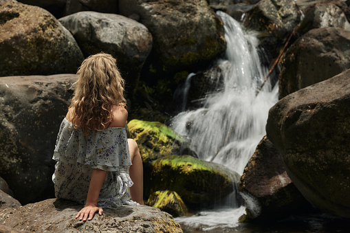 Rear view of a woman relaxing on the rocks by the waterfall.