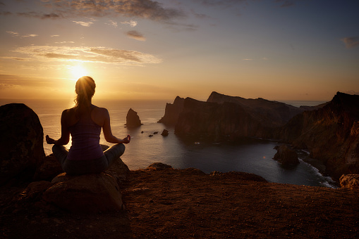 Rear view of athletic woman doing Yoga relaxation exercises on coastline of Ponta De Sao Lourenco at sunset. Copy space.