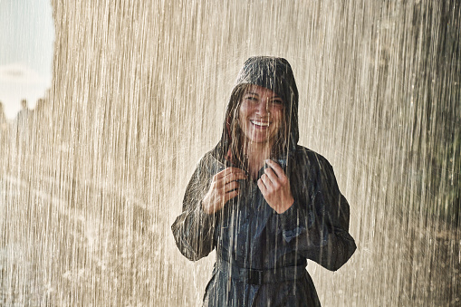 Happy woman in raincoat enjoying while standing on rain in nature and looking at camera. Copy space.