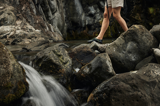 Unrecognizable female tourist walking on rocks by the waterfall in nature.
