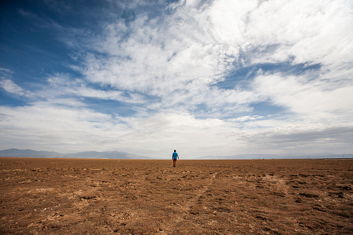 A man standing alone in an empty and flat field.