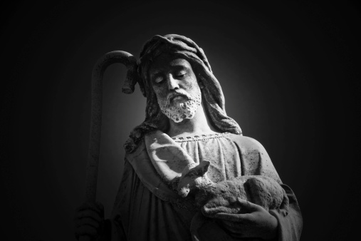 Black and white old statue of Jesus christ with lamb and walking stick,against black background, full frame horizontal composition with copy space and vignette