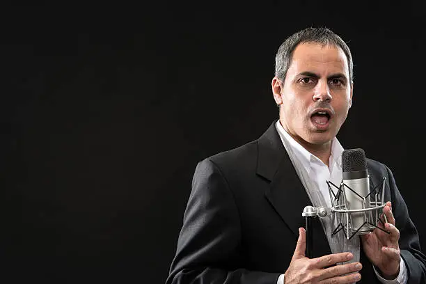 Middle eastern man in front of a microphone on black background