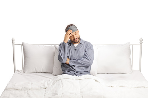 Sad man in pajamas sitting in a bed and thinking isolated on white background