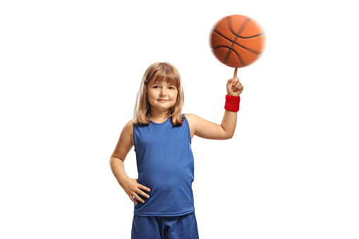 Smiling little girl in a blue jersey spinning a basketball with her finger isolated on white background