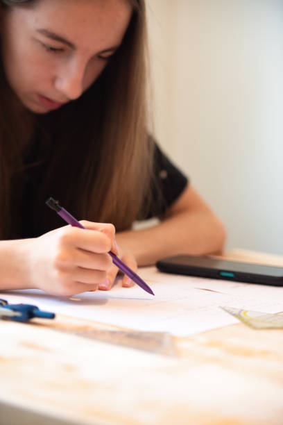 istock Teenage Girl at Home Sitting at Kitchen Table Working on Math Homework 1714565987