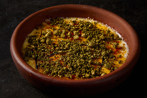 Close-up horizontal side view of crÃ¨me brÃ»lÃ©e with pistachio, emphasizing its creamy texture and caramelized surface, set against a dark ambiance.