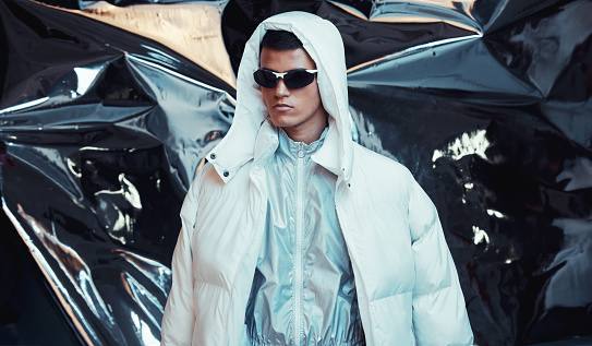 Holographic, sci fi and man with fashion and futuristic ski style with vaporwave clothing in studio. Art, creative and young male model with trendy, cool sunglasses and cyberpunk designer jacket