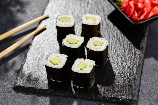 istock Avocado hosomaki on dark stone table. Hosomaki with avocado. Sushi roll with avocado inside. Style concept japanese menu with black background, leaves and hard shadow. 1714577480