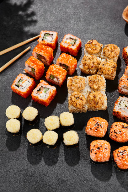 istock Maki sushi set on dark background. Maki set with variety rolls. Composition from sushi rolls and baked maki . Style concept sushi menu with black background, leaves and hard shadow. 1714577525