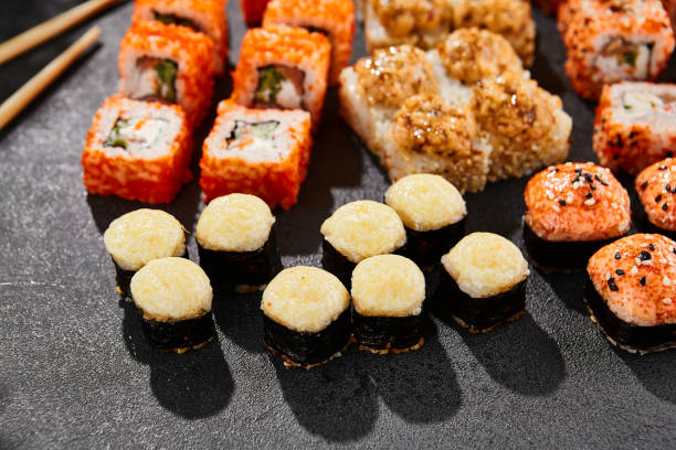 istock Maki sushi set on dark background. Maki set with variety rolls. Composition from sushi rolls and baked maki . Style concept sushi menu with black background, leaves and hard shadow. 1714577532