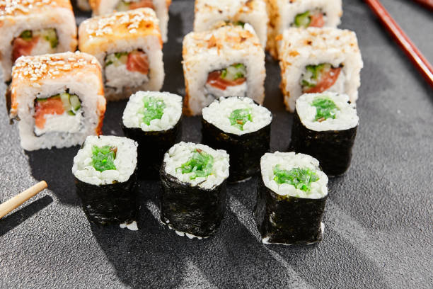 istock Maki sushi set on dark background. Maki set with variety rolls. Composition from popular sushi rolls and hosomaki. Style concept sushi menu with black background, leaves and hard shadow. 1714577539