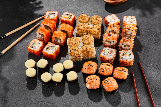 istock Maki sushi set on dark background. Maki set with variety rolls. Composition from sushi rolls and baked maki . Style concept sushi menu with black background, leaves and hard shadow. 1714577554