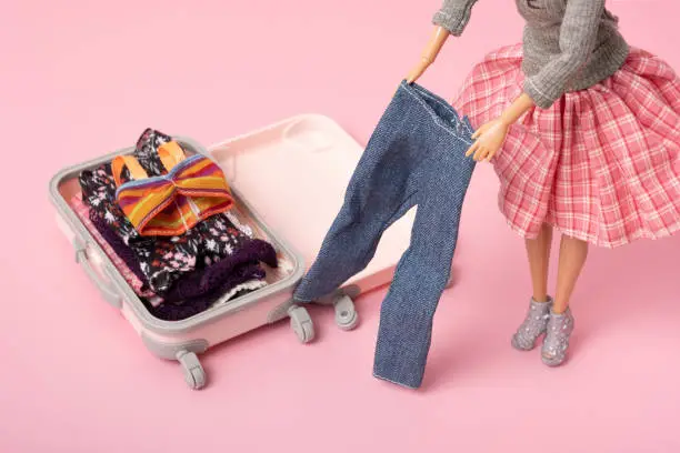 The doll puts clothes in a suitcase, prepares luggage. Travel, vacation creative minimalistic concept