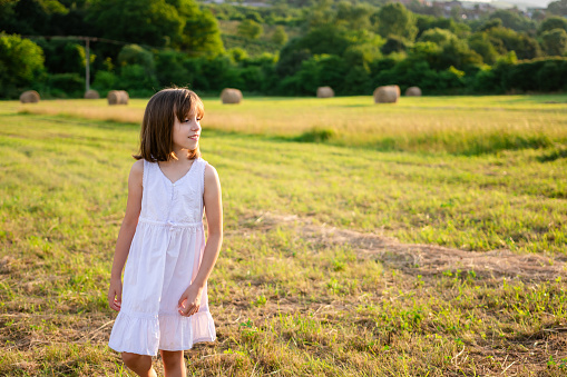 Happy little girl walking in a field with hay bales on a summer day