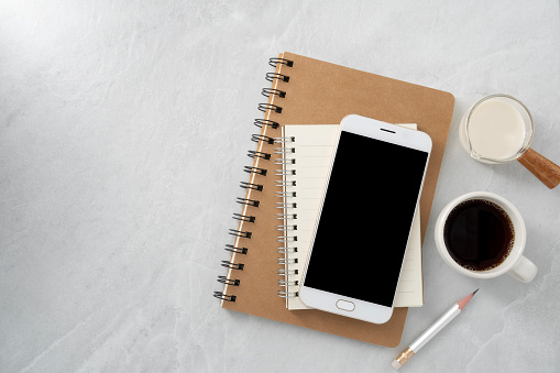 Mobile phone with blank mockup screen and book and coffee on stone texture background.Work desk. Top view. Flat lay.