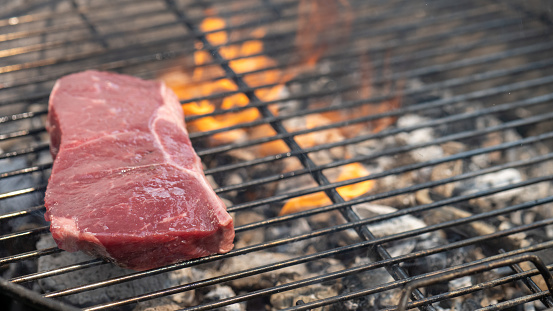 Close-up of a raw beef steak roasting on a barbecue grill.