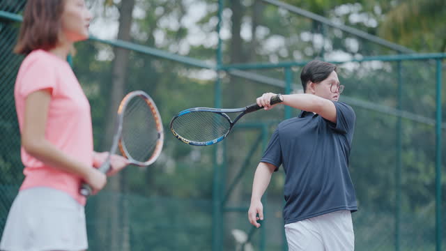 Asian Chinese Down syndrome man learning from female coach trainer playing tennis during weekend morning
