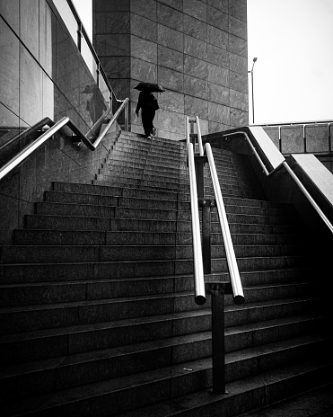 Woman walking up stairs in the rain while holding an umbrella