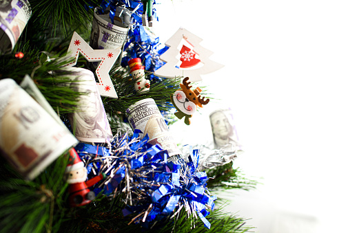 Detail of christmas tree with decorations and dollar bills wishing to earn money in the new year eve, with blank copy space.