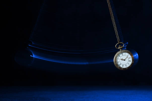 istock Hypnosis session. Vintage pocket watch with chain swinging over surface on dark background among faded clock faces, magic motion effect 1714624428