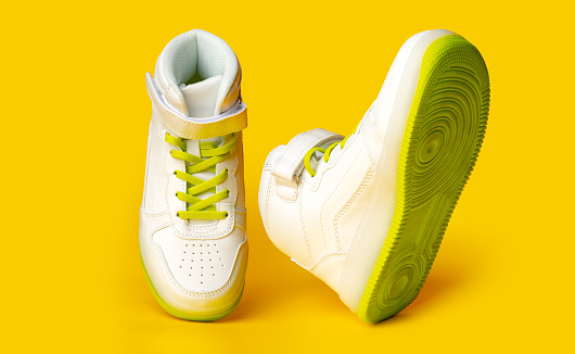 White sneakers with yellow neon laces on yellow studio background
