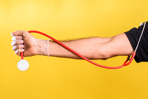 Doctor holds in his hand a stethoscope, isolated on yellow studio background.