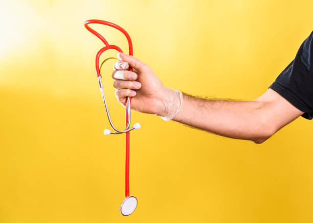 Doctor holds in his hand a stethoscope, isolated on yellow studio background.