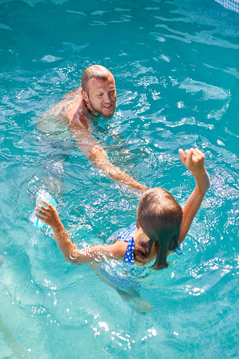 Father and daughter have fun in swimpool at home on the backyard, summer time, outdoor