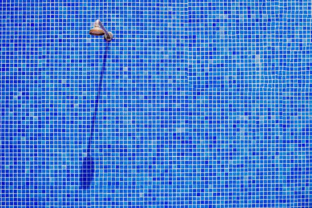 Old shower head without water for bathers in a swimming pool, on a wall of blue tiles in the sun.