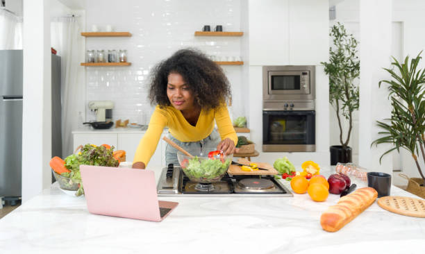 istock Young woman utilizing digital recipes from laptop computer. Cooking preparation in modern kitchen. 1714675928