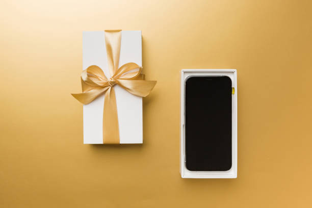 istock Opened gift box with gold ribbon and smartphone on color background, top view. Blank open box packaging mockup , Template for your design - branding mockup 1714684484