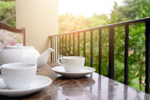 White teapot and cup of tea on table. Outdoor breakfast on balcony cafe