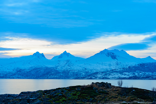 Snowy winter landscape sunset at the shore of the Vestfjord from one of the islands of the Vesteralen archipel near Lodingen in Norway The mountains are covered in snow and there clouds floating over the mountains in the distance.