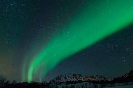 Northern Lights, polar light or Aurora Borealis in the night sky over the Lofoten islands in Northern Norway. Wide panoramic image with snow covered mountains and a lake in the foreground.