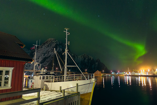 Northern Lights, polar light or Aurora Borealis in the night sky over the port of Svolvaer in the Lofoten in Nordland Norway. A fishing boat is moored in front of a cabin.