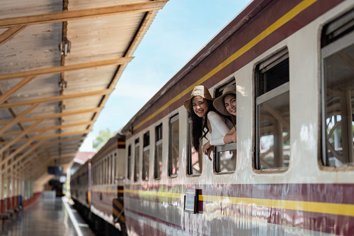 Young woman travelling by train and waving her hand out window.