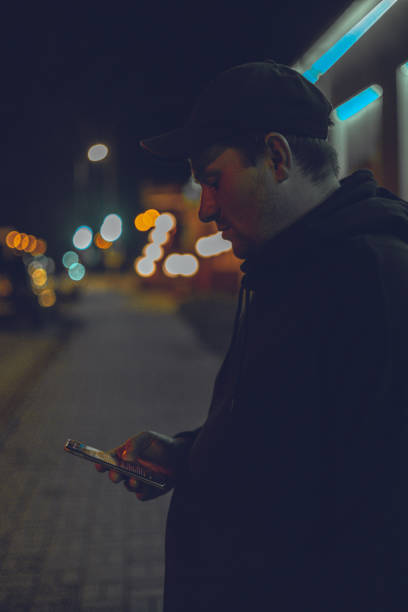 um homem está na rua de uma cidade noturna sob luz de néon. cyberpunk. um homem segura um telefone na mão na luz neon das luzes noturnas em uma rua da cidade. conceito de vida noturna. - beautiful outdoors vertical close up - fotografias e filmes do acervo