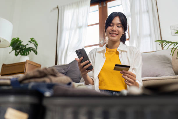 szczęśliwa młoda kobieta z kartą kredytową rezerwującą wakacje w biurze podróży lub dokonującą rezerwacji hotelu online - national cash register zdjęcia i obrazy z banku zdjęć