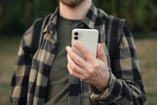 istock Man using white smartphone on blurred nature background, close up. 1714757052