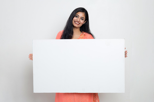 Indian woman in ethnic wear holding white sign board in hand and looking towards the camera , Advisement concept