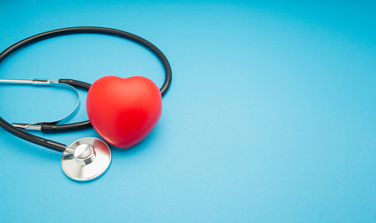 Top view of a stethoscope and a red heart shape on a blue background. Space for text. Medical and healthcare concept