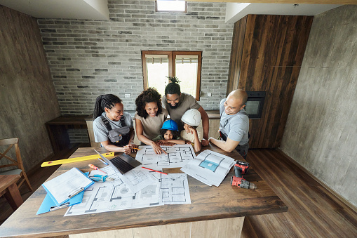 High angle view of happy African American family and manual workers examining renovation plans inside of a house. Copy space.