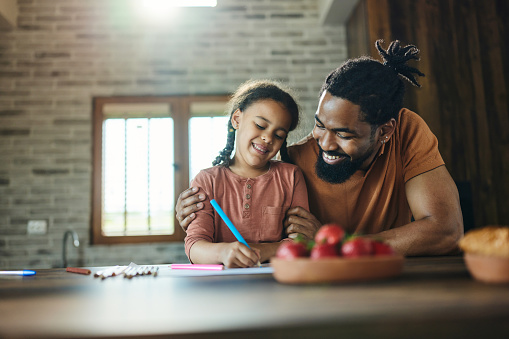 Happy African American single father and his small daughter making a drawing at home.